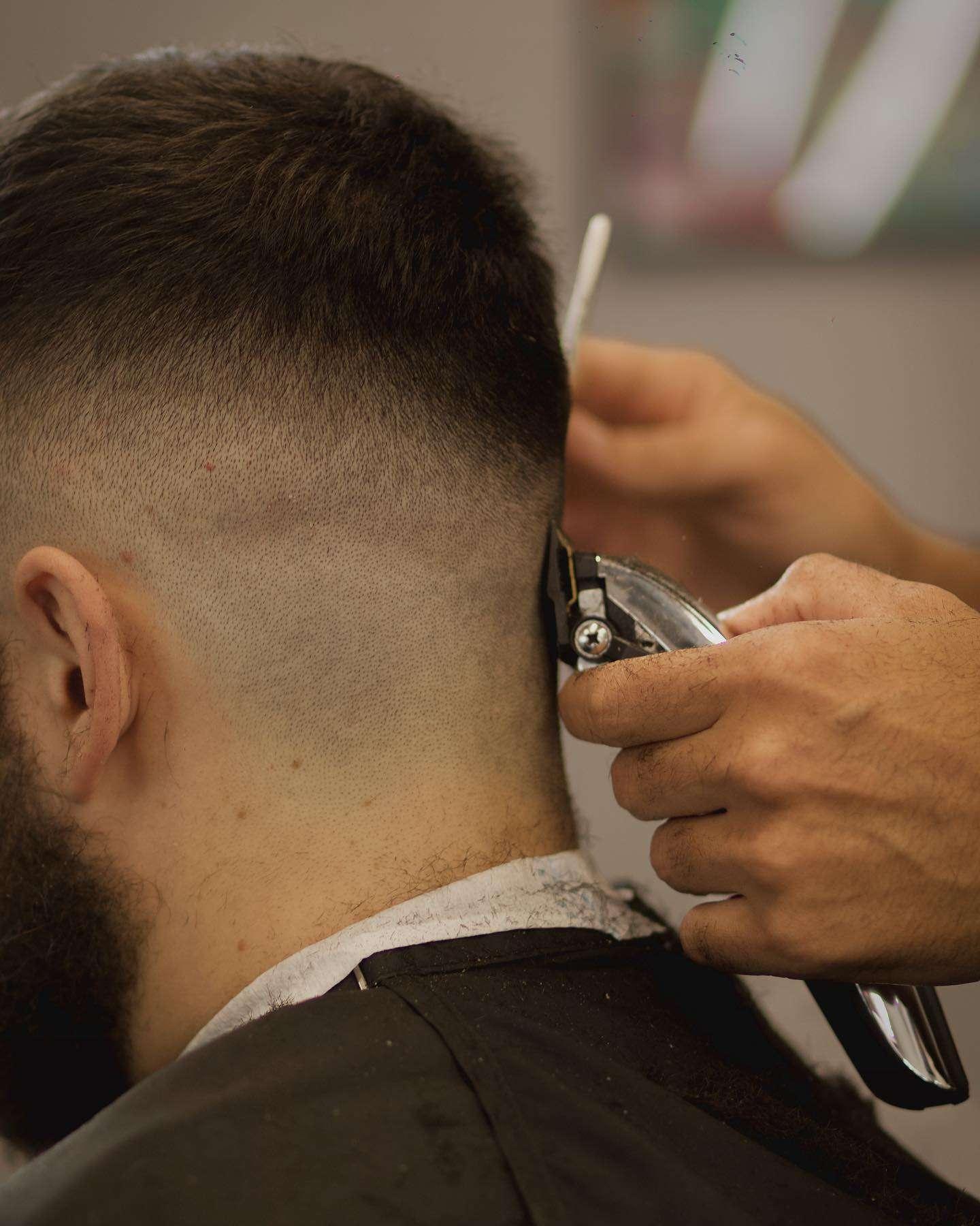 A barber giving a close fade haircut to a man using electric clippers, focusing on the back of the head where the hair gradually transitions from short to skin.