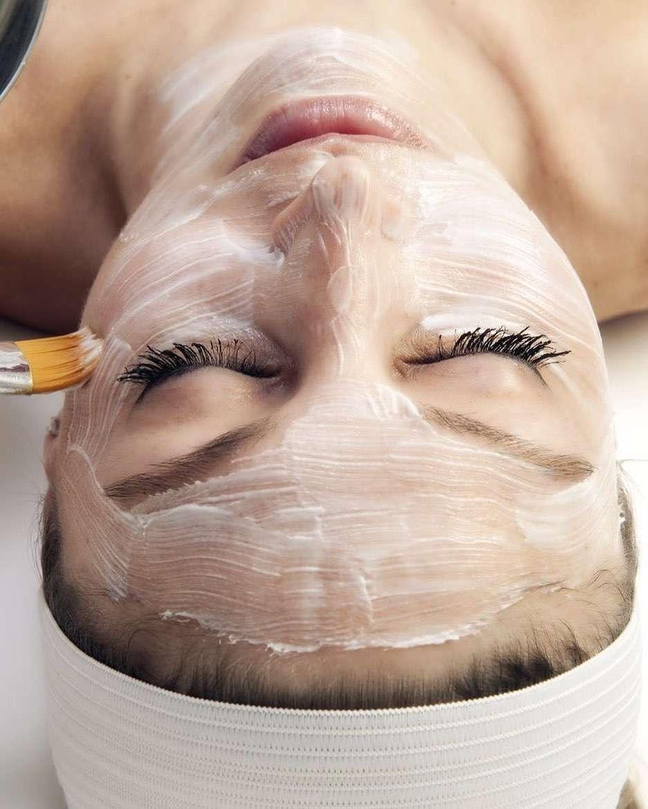 Woman lying down with eyes closed while a facial mask is applied with a brush across her face.
